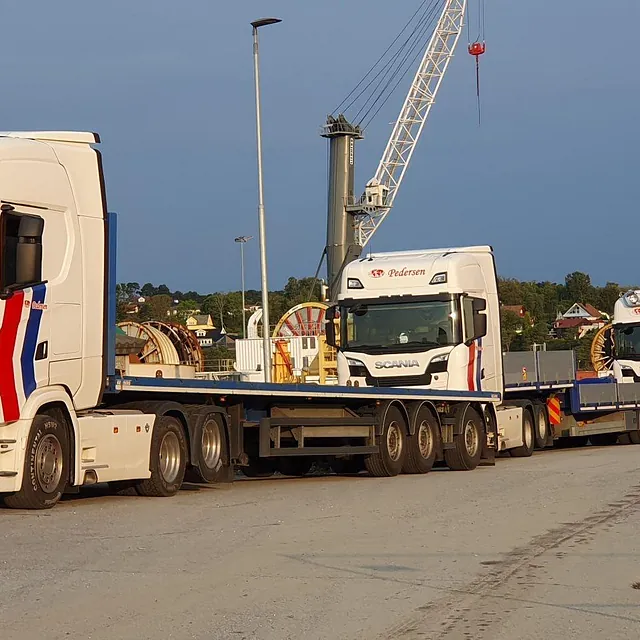 Tre hvite lastebiler med Pedersen-logo står parkert på et industriområde ved havn.