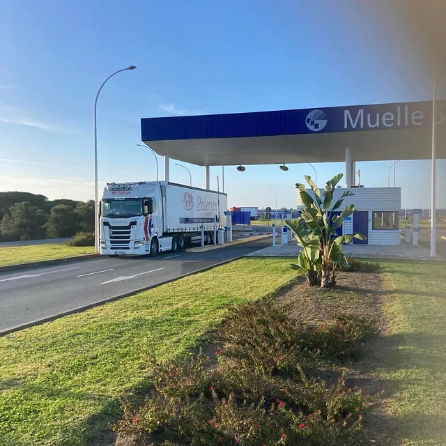 En Pedersen-lastebil passerer en tollstasjon merket «Muelle Sur» under blå himmel.