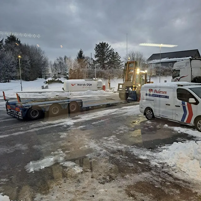 Truck laster en tilhenger i snødekt område med Pedersen-kjøretøy og tanken «Norsk Olje».